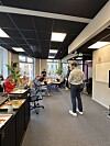 Gruppe samlet i et kontorlandskap med bord, skjermer og folk som sitter og står i møte.